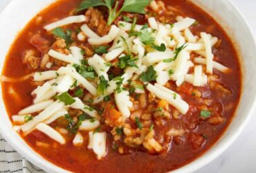 Crockpot Stuffed Pepper Soup served in a white bowl with a spoon, garnished with fresh parsley and shredded cheese on a rustic wooden table