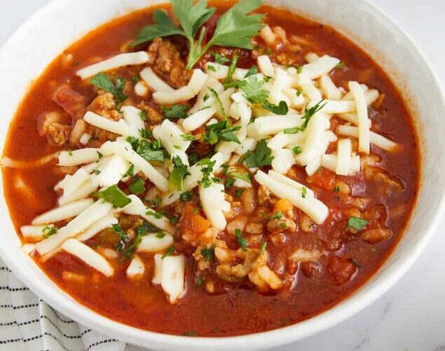 Crockpot Stuffed Pepper Soup served in a white bowl with a spoon, garnished with fresh parsley and shredded cheese on a rustic wooden table