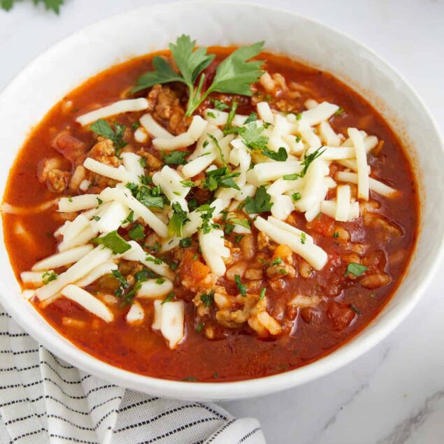 Crockpot Stuffed Pepper Soup served in a white bowl with a spoon, garnished with fresh parsley and shredded cheese on a rustic wooden table