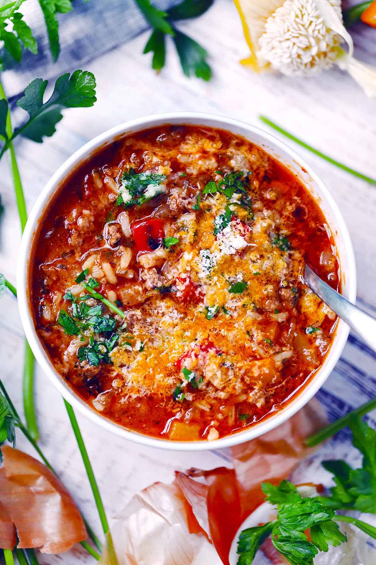 Overhead flat lay of crockpot stuffed pepper soup ingredients including ground beef, diced bell peppers, canned tomatoes, uncooked white rice, and seasonings arranged on a light surface