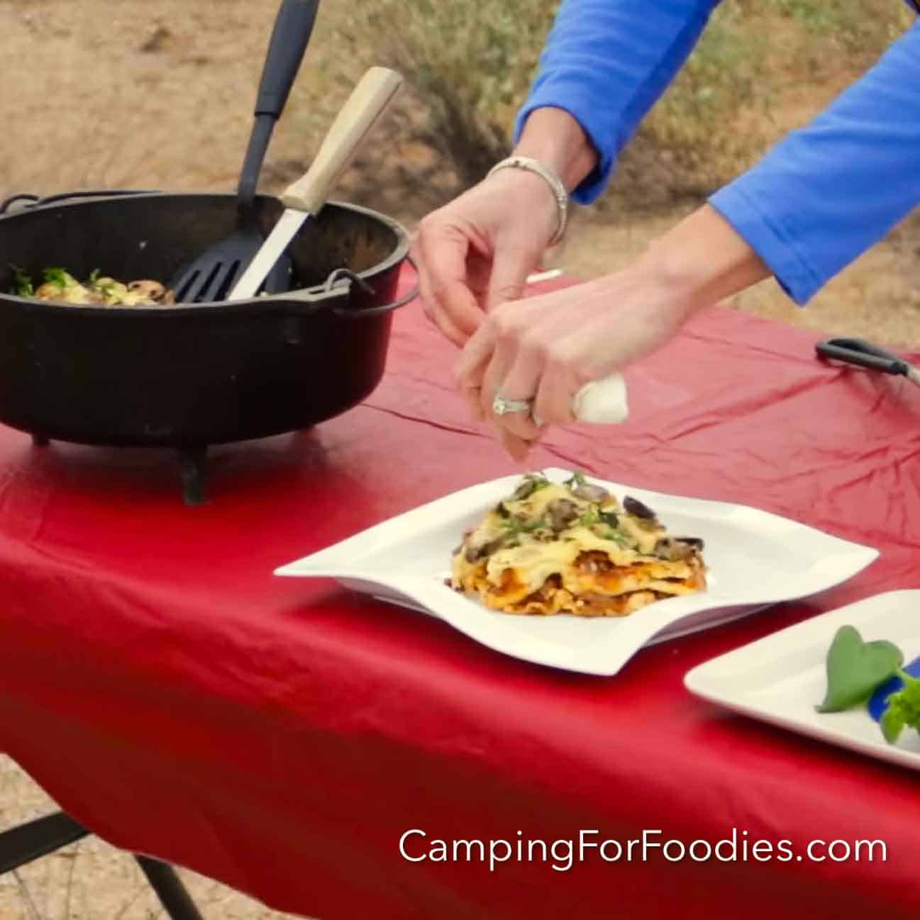 Dutch Oven Lasagna ingredients laid out flat — no-boil noodles, ricotta, mozzarella, Italian sausage, and jarred marinara on a rustic camp table