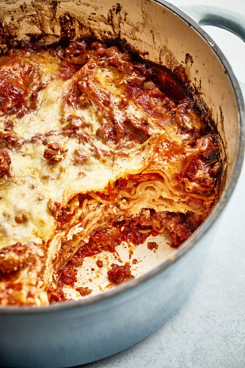 Close-up of a serving of Dutch Oven Lasagna being lifted with a spatula, showing gooey melted cheese and rich sausage meat sauce layers