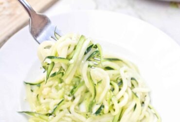 Garlic Parmesan Zoodles beautifully plated in a white pasta bowl, topped with freshly grated Parmesan, cracked black pepper, and fresh basil, shot overhead on a rustic wood surface