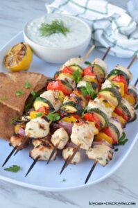 Grilled Chicken Skewers with Tzatziki served on a wooden board with warm pita, fresh cucumber slices, lemon wedges, and a generous bowl of creamy tzatziki sauce