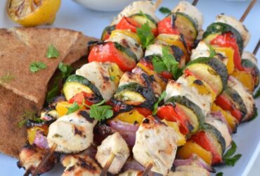 Grilled Chicken Skewers with Tzatziki served on a wooden board with warm pita, fresh cucumber slices, lemon wedges, and a generous bowl of creamy tzatziki sauce