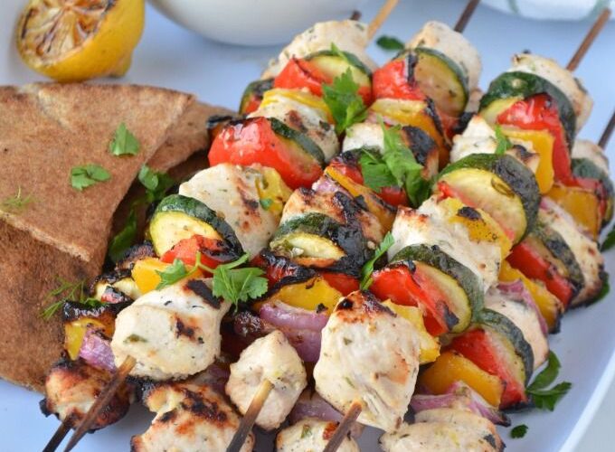 Grilled Chicken Skewers with Tzatziki served on a wooden board with warm pita, fresh cucumber slices, lemon wedges, and a generous bowl of creamy tzatziki sauce
