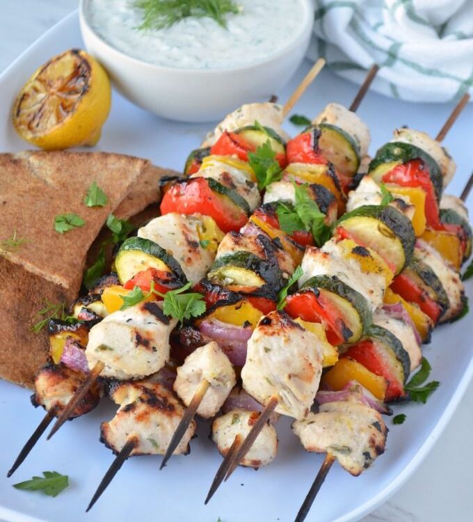 Grilled Chicken Skewers with Tzatziki served on a wooden board with warm pita, fresh cucumber slices, lemon wedges, and a generous bowl of creamy tzatziki sauce
