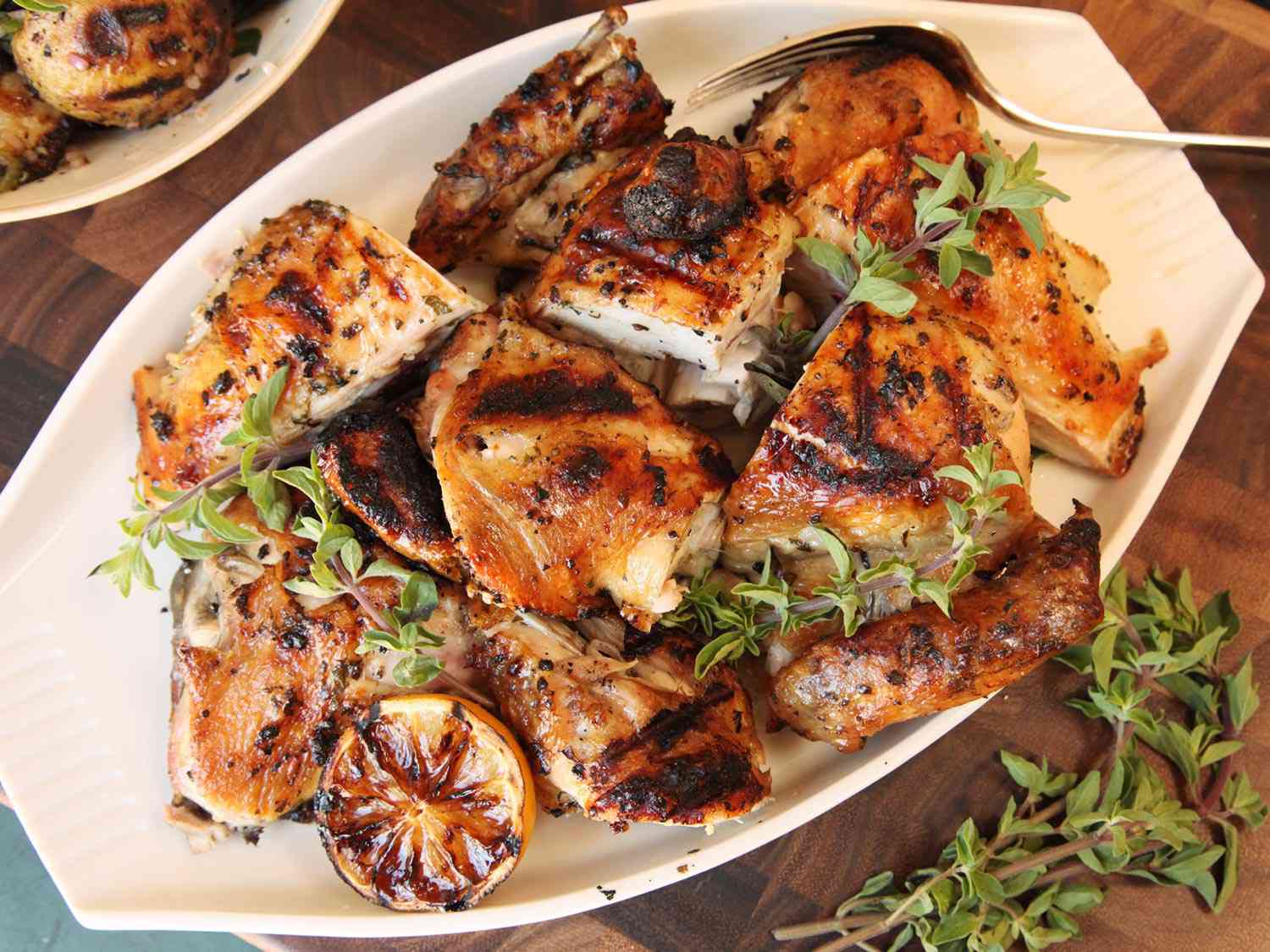 Flat lay of grilled chicken skewer ingredients — raw chicken thighs, garlic cloves, lemon halves, fresh herbs, olive oil, and a bowl of Greek yogurt on a marble surface