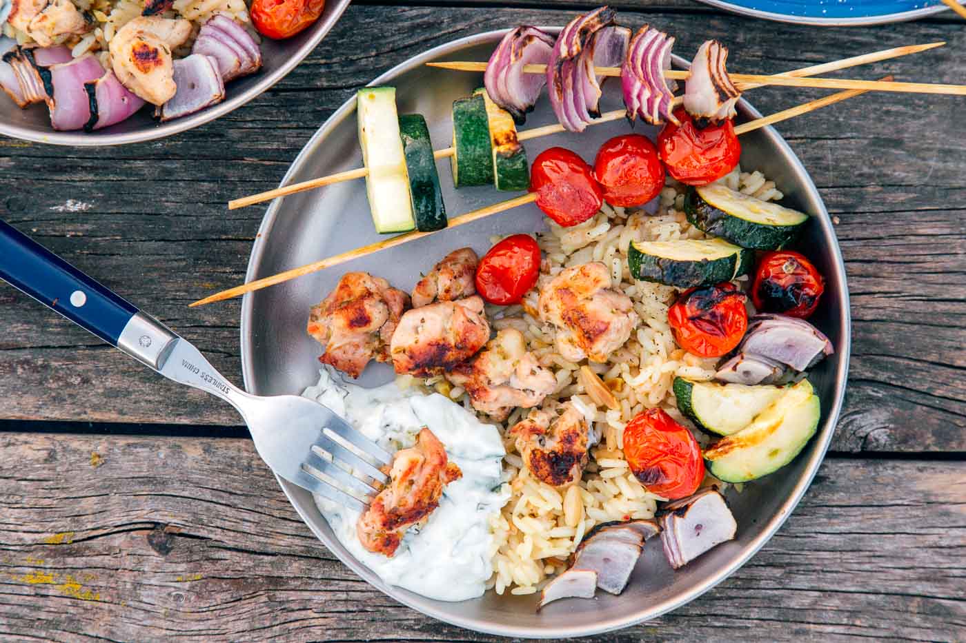 Close-up of grilled chicken skewers resting on a rustic wooden board, garnished with fresh dill, a drizzle of olive oil, and a small bowl of tzatziki alongside sliced pita wedges