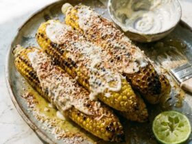 Grilled corn on the cob elote style with charred kernels, Parmesan, chili butter, and lime wedges on a rustic wooden board