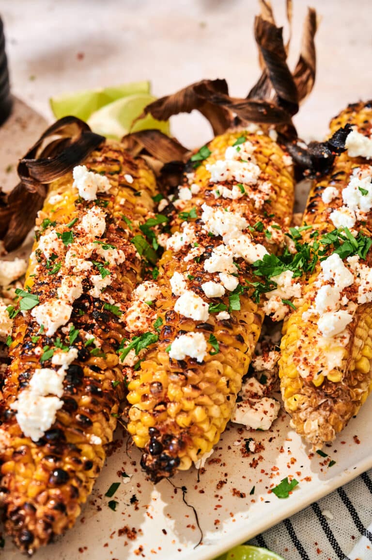 Close-up of charred grilled corn on the cob with melted garlic butter, Parmesan, chili powder, and fresh lime wedge on a dark plate