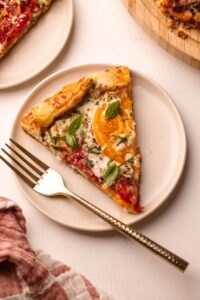 A beautifully plated heirloom tomato galette on a wooden serving board, golden flaky crust folded over vibrant red and yellow heirloom tomato slices, garnished with fresh basil leaves and a drizzle of olive oil