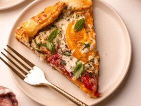 A beautifully plated heirloom tomato galette on a wooden serving board, golden flaky crust folded over vibrant red and yellow heirloom tomato slices, garnished with fresh basil leaves and a drizzle of olive oil