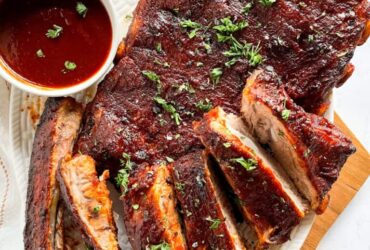 Instant Pot ribs plated on a wooden board with BBQ sauce glaze, charred edges, and fresh herbs garnish