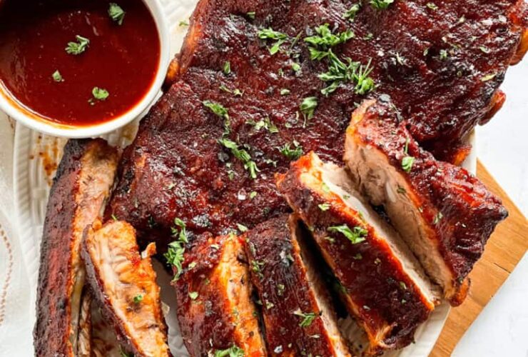 Instant Pot ribs plated on a wooden board with BBQ sauce glaze, charred edges, and fresh herbs garnish