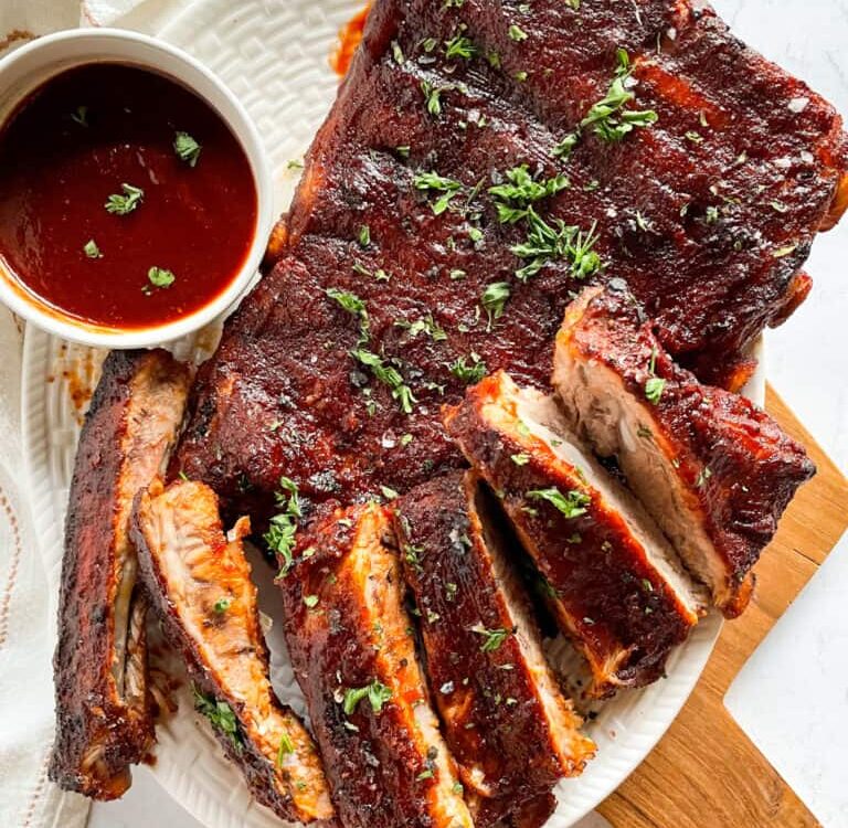 Instant Pot ribs plated on a wooden board with BBQ sauce glaze, charred edges, and fresh herbs garnish
