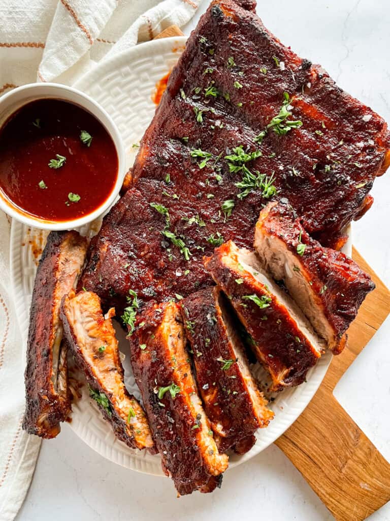 Instant Pot ribs plated on a wooden board with BBQ sauce glaze, charred edges, and fresh herbs garnish