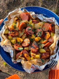 Kielbasa and potato foil packets opened on a plate showing smoky sausage slices, golden potatoes, and a glossy butter and spicy mustard glaze, garnished with fresh parsley