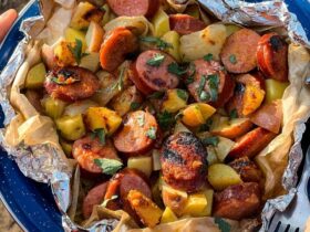 Kielbasa and potato foil packets opened on a plate showing smoky sausage slices, golden potatoes, and a glossy butter and spicy mustard glaze, garnished with fresh parsley