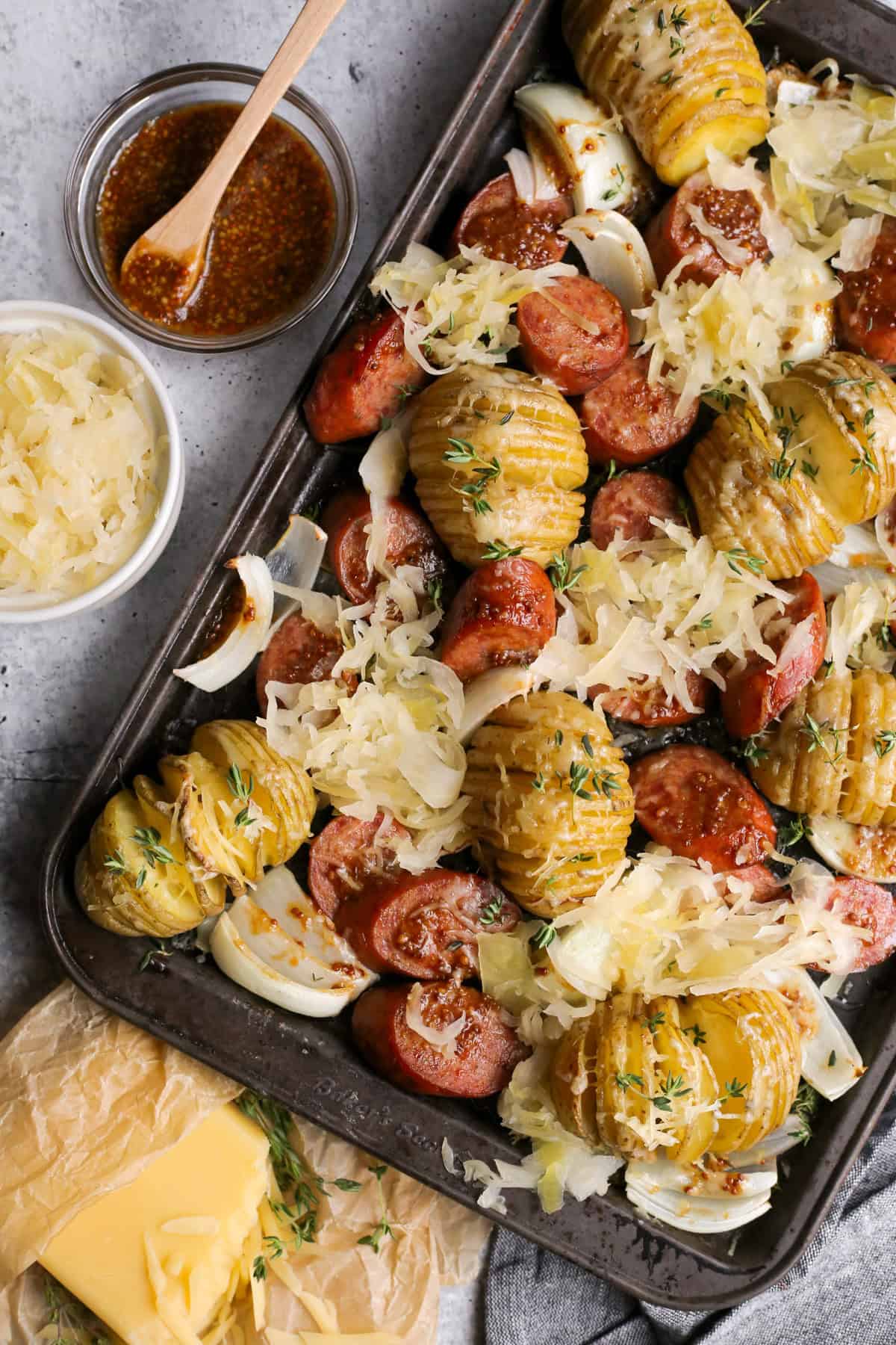 Overhead flat-lay of kielbasa slices, diced Yukon Gold potatoes, pats of butter, spicy mustard, and foil sheets arranged on a wooden cutting board before assembling the packets