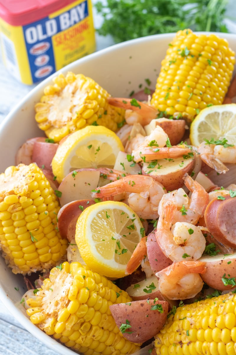 Close-up of Low Country Shrimp Boil in a rustic bowl with melted butter drizzle, lemon wedge, fresh parsley, and visible corn kernels and sausage slices