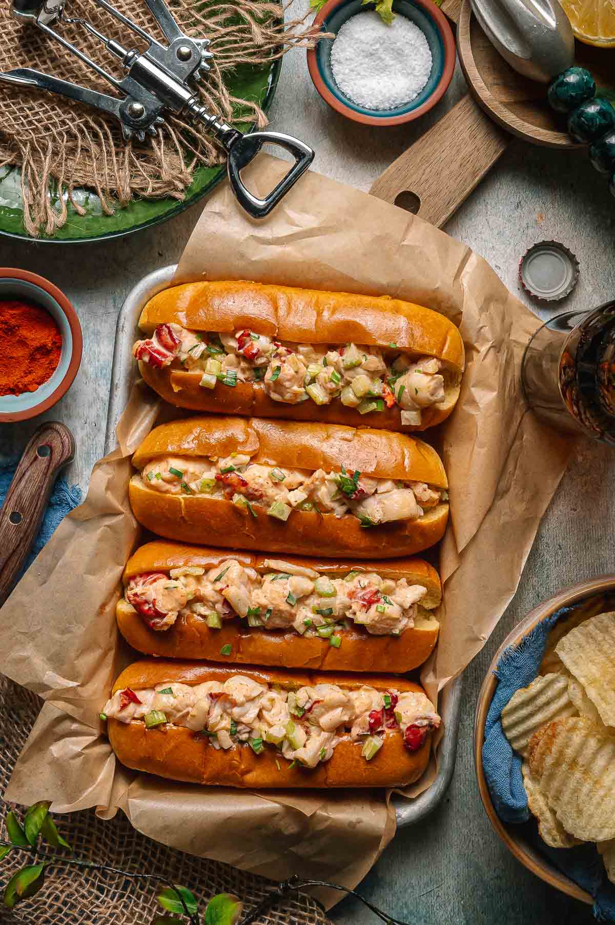 Classic Maine Lobster Rolls served in golden buttered split-top hot dog buns, piled high with creamy lobster salad, garnished with fresh chives and lemon wedges on a rustic wooden board