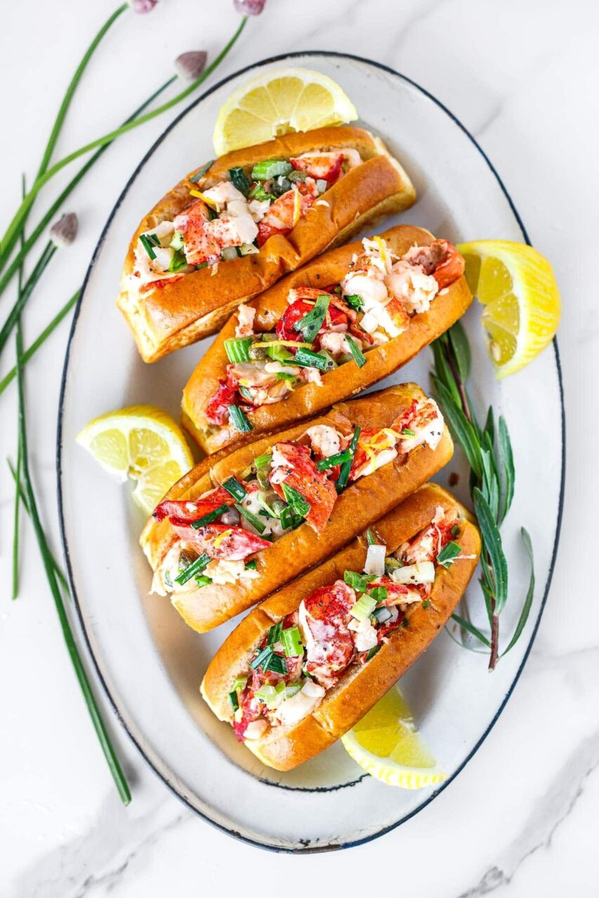 Step-by-step flat lay showing raw lobster tails, a bowl of creamy lobster salad with celery and lemon, and split-top buns being toasted in a buttered skillet
