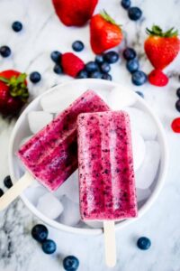 Mixed Berry Popsicles made with real strawberries, blueberries, and raspberries arranged on a bed of crushed ice with fresh berries scattered around
