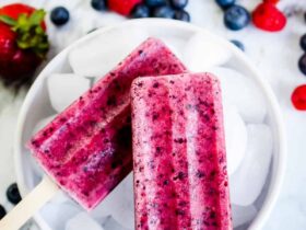 Mixed Berry Popsicles made with real strawberries, blueberries, and raspberries arranged on a bed of crushed ice with fresh berries scattered around