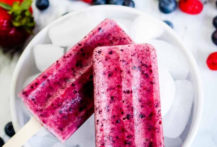 Mixed Berry Popsicles made with real strawberries, blueberries, and raspberries arranged on a bed of crushed ice with fresh berries scattered around