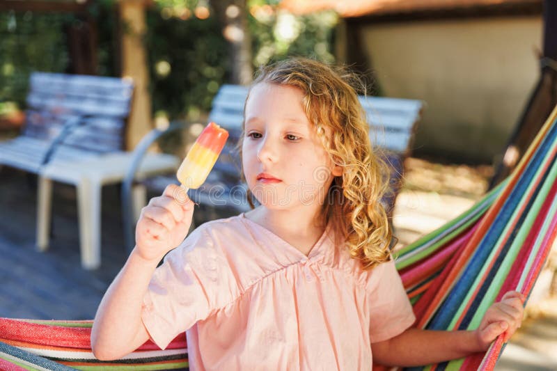 Close-up of a Mixed Berry Popsicle being held by a child's hand against a sunny outdoor background with bite taken out revealing vibrant purple-red fruit interior