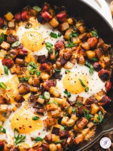 One pan camping breakfast skillet with eggs, crispy potatoes, colorful peppers and sausage in a cast iron pan, served hot and golden