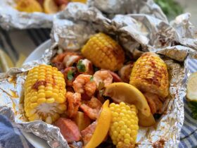 Shrimp boil foil packets opened on a wooden board showing shrimp, smoked sausage, corn, and potatoes with melted butter and parsley