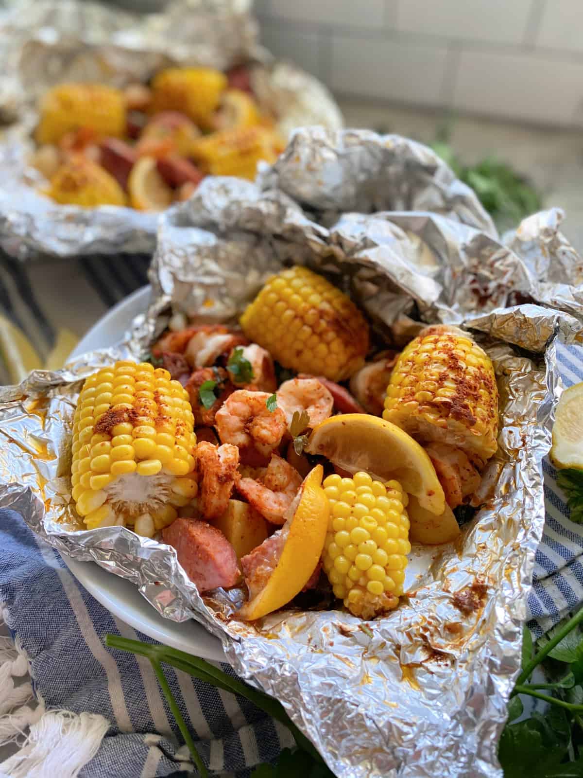 Shrimp boil foil packets opened on a wooden board showing shrimp, smoked sausage, corn, and potatoes with melted butter and parsley
