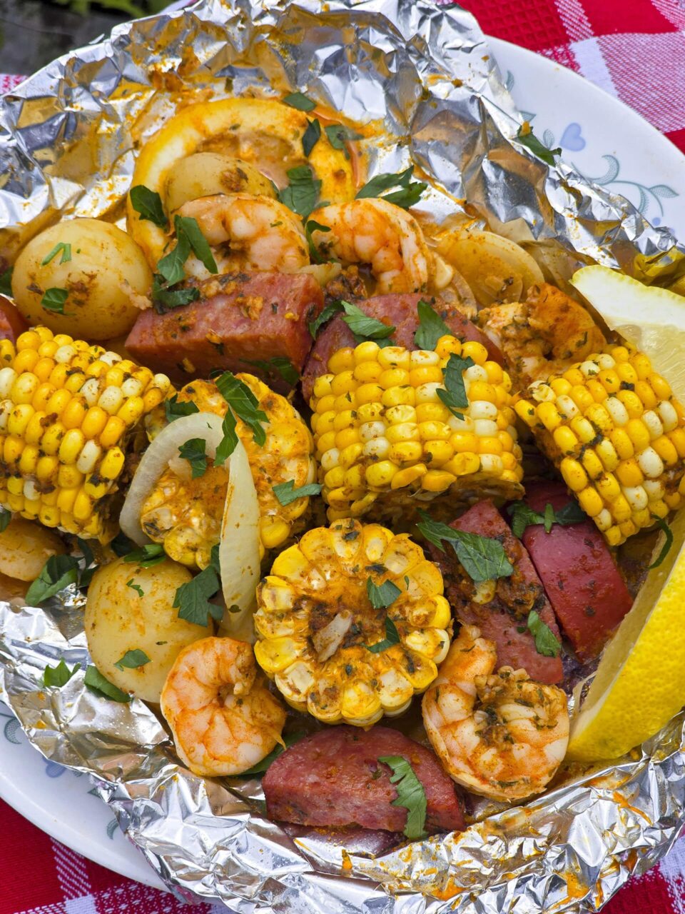 Flat lay of shrimp boil foil packet ingredients — raw shrimp, sliced sausage, corn rounds, baby potatoes, butter, and Cajun seasoning on a kitchen counter