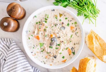 Slow cooker chicken wild rice soup served in a rustic white bowl, garnished with fresh thyme and cracked black pepper, with a spoon resting on the side