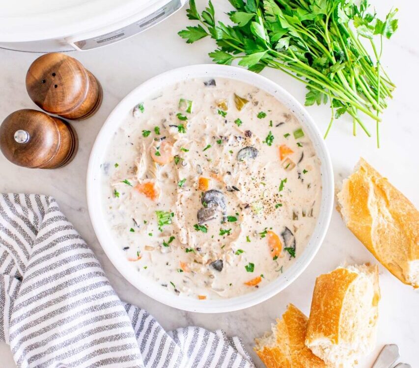 Slow cooker chicken wild rice soup served in a rustic white bowl, garnished with fresh thyme and cracked black pepper, with a spoon resting on the side