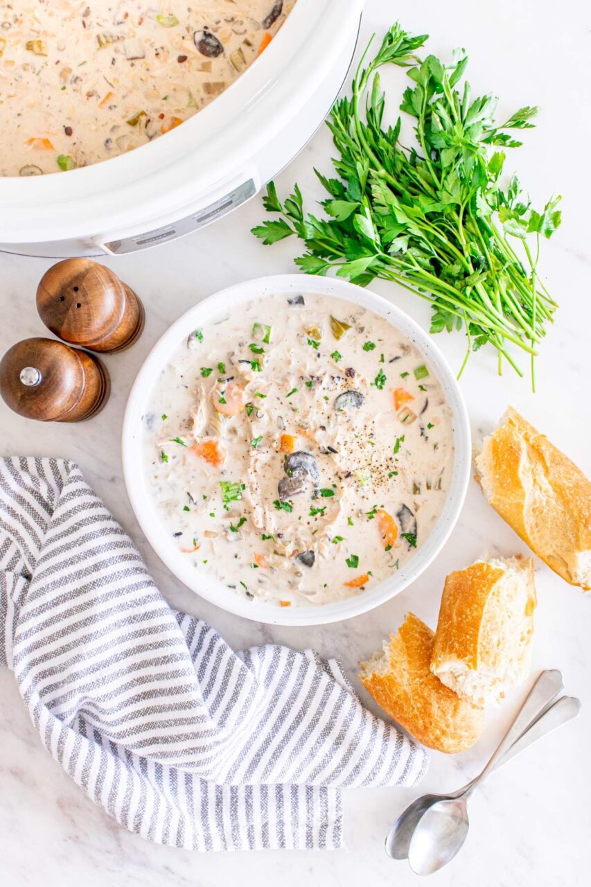 Slow cooker chicken wild rice soup served in a rustic white bowl, garnished with fresh thyme and cracked black pepper, with a spoon resting on the side