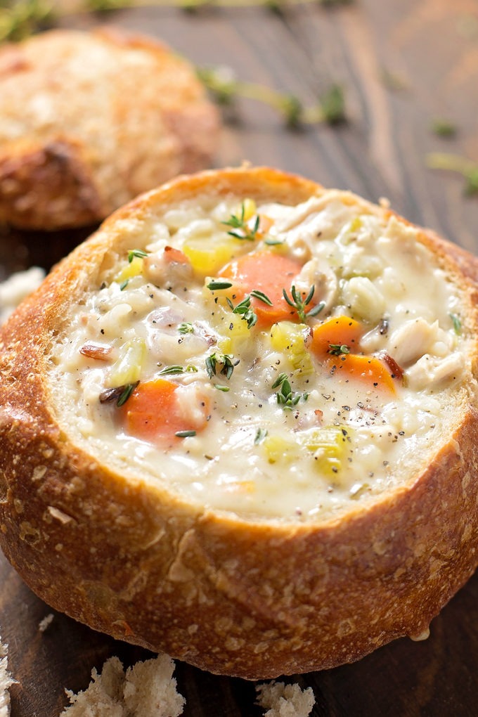 Close-up overhead shot of a steaming bowl of slow cooker chicken wild rice soup with shredded chicken, wild rice grains, and diced vegetables visible, topped with fresh thyme sprigs and served alongside crusty bread
