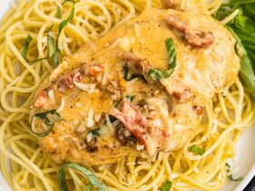 Slow Cooker Marry Me Chicken served over fettuccine pasta on a white plate, garnished with fresh basil and Parmesan, photographed from slightly above with a rustic linen napkin and fork