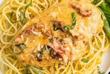 Slow Cooker Marry Me Chicken served over fettuccine pasta on a white plate, garnished with fresh basil and Parmesan, photographed from slightly above with a rustic linen napkin and fork