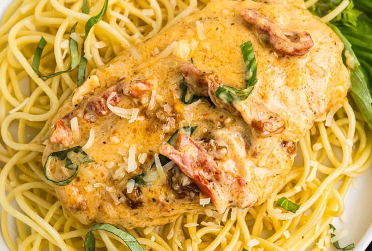 Slow Cooker Marry Me Chicken served over fettuccine pasta on a white plate, garnished with fresh basil and Parmesan, photographed from slightly above with a rustic linen napkin and fork