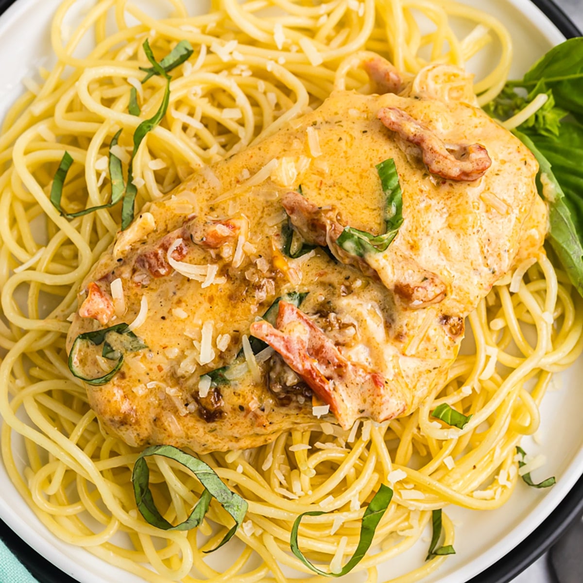 Slow Cooker Marry Me Chicken served over fettuccine pasta on a white plate, garnished with fresh basil and Parmesan, photographed from slightly above with a rustic linen napkin and fork