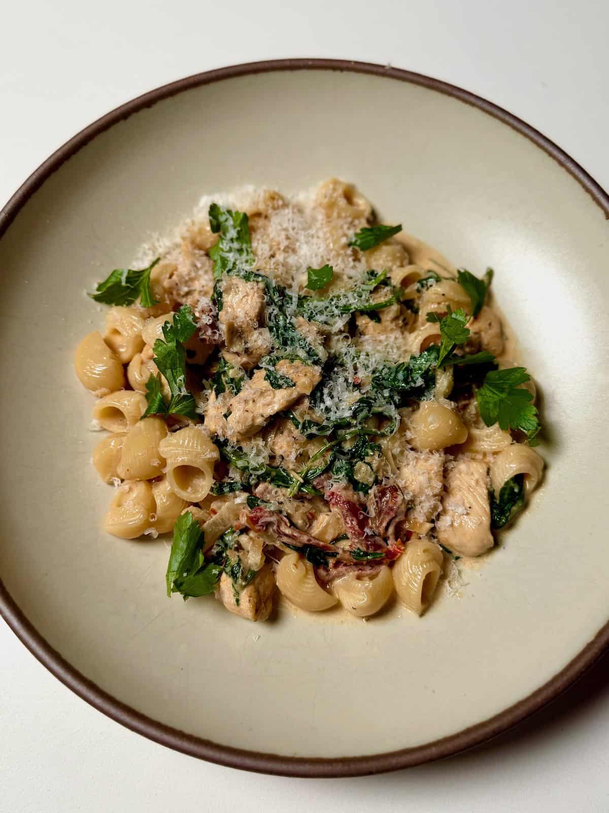 Close-up of Slow Cooker Marry Me Chicken sauce being spooned over fettuccine pasta in a shallow bowl, showing the creamy texture, sun-dried tomato pieces, and fresh basil garnish in warm natural light