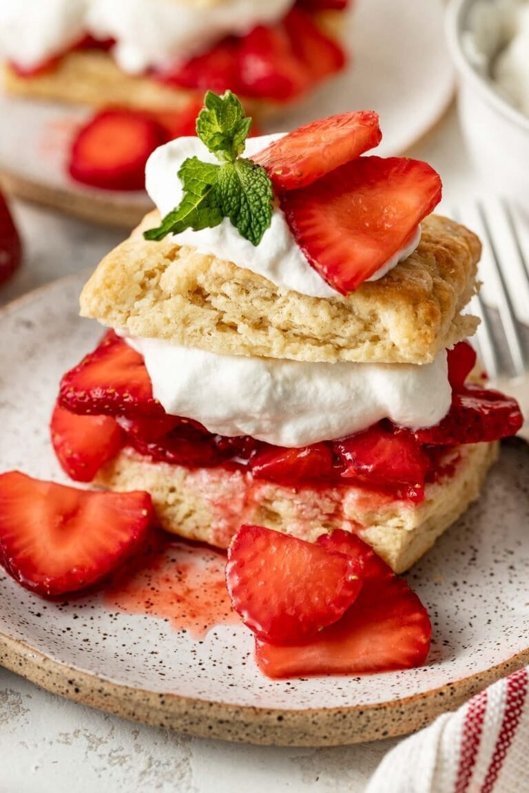 Close-up of a single strawberry shortcake serving — biscuit split open and overflowing with glossy macerated strawberries and a generous swirl of whipped cream, natural light photography
