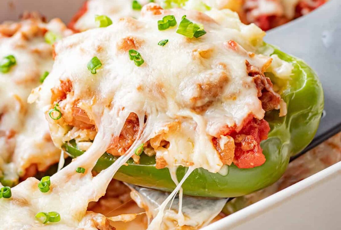 Stuffed bell peppers filled with seasoned ground beef, rice, and melted cheese, arranged in a white baking dish on a wooden table, garnished with fresh parsley