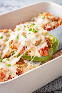Stuffed bell peppers filled with seasoned ground beef, rice, and melted cheese, arranged in a white baking dish on a wooden table, garnished with fresh parsley
