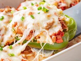 Stuffed bell peppers filled with seasoned ground beef, rice, and melted cheese, arranged in a white baking dish on a wooden table, garnished with fresh parsley