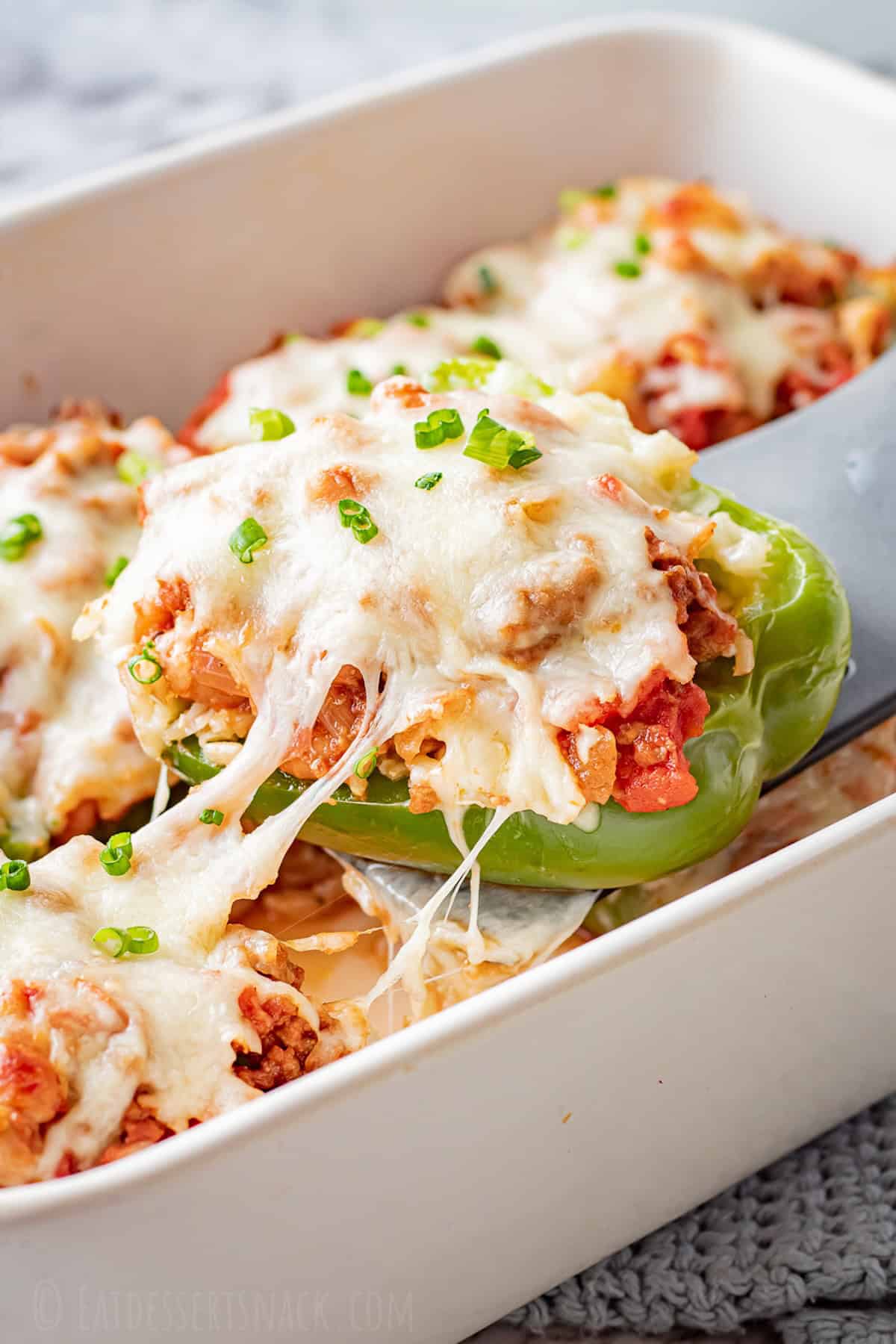 Stuffed bell peppers filled with seasoned ground beef, rice, and melted cheese, arranged in a white baking dish on a wooden table, garnished with fresh parsley