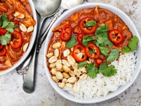 Sweet potato peanut stew served in a wide bowl over white rice, garnished with chopped cilantro and a lime wedge, warm overhead shot on a rustic wooden table